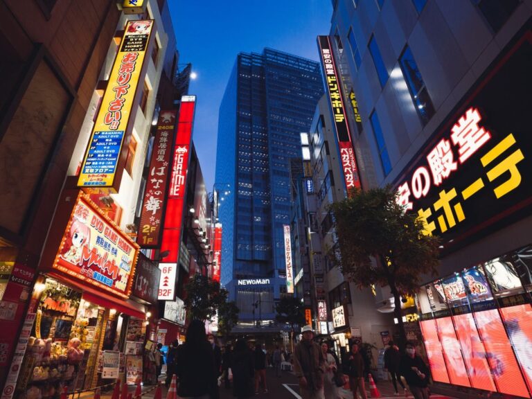 Street view of Tokyo's bustling nightlife with illuminated storefronts and skyscrapers.
