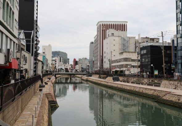 Serene view of a city canal in Fukuoka, Japan, flanked by modern architecture and reflective waters.