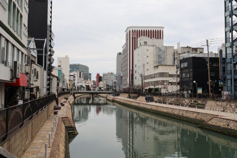 Serene view of a city canal in Fukuoka, Japan, flanked by modern architecture and reflective waters.